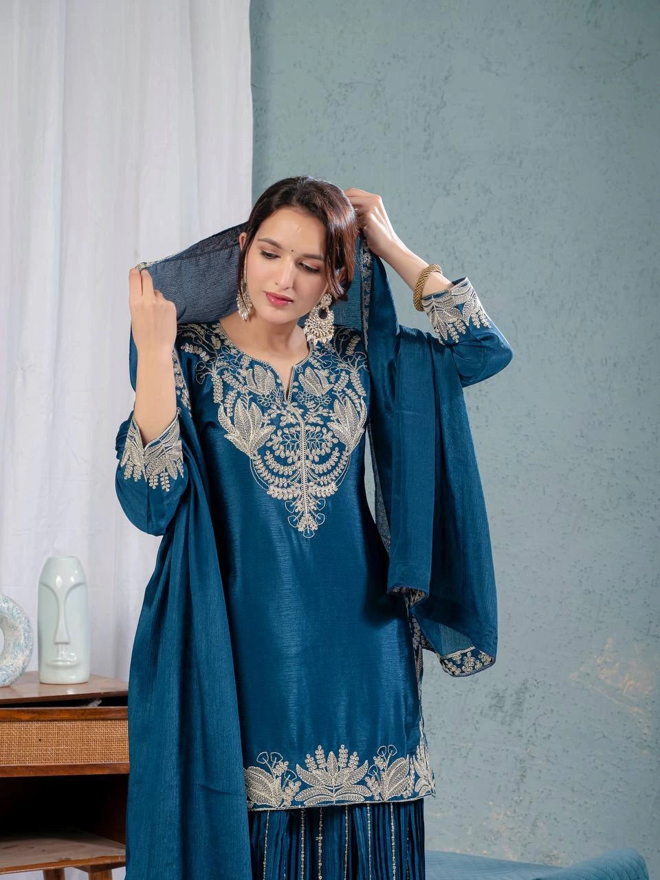Woman wearing a blue embroidered outfit with a gray curtain background